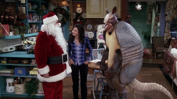 Ross Geller dressed as the Holiday Armadillo standing next to Santa and Superman.