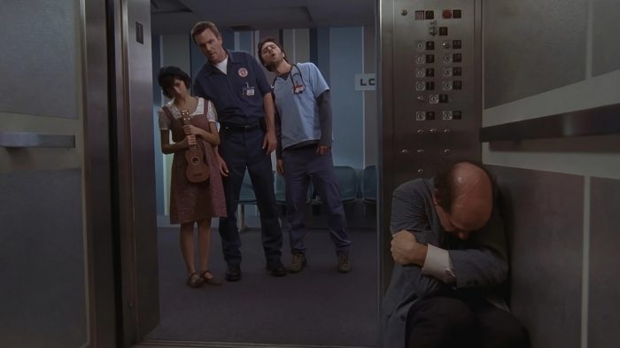 Ted Buckland sitting curled up in an elevator while the Janitor, Gooch, and JD look on.