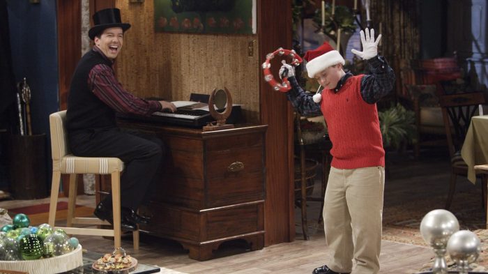 Jack McFarland wearing a top hat and playing the piano while his nephew Jordy performs with a tambourine in a Santa hat.